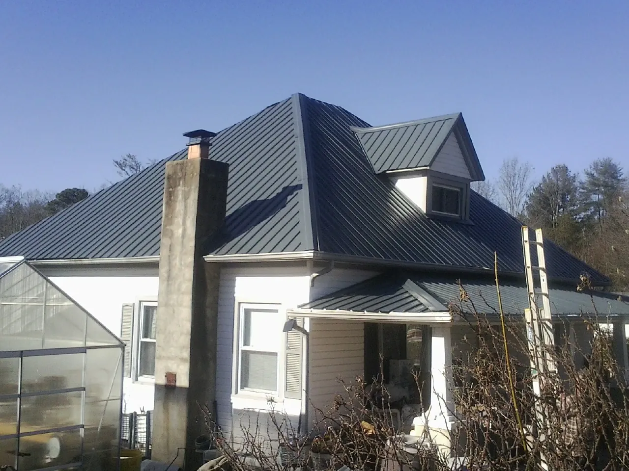 Dark blue standing seam metal roof on a white farmhouse with dormer — Slate & Tile Roof Repair by Roofing Brothers in Lapaz