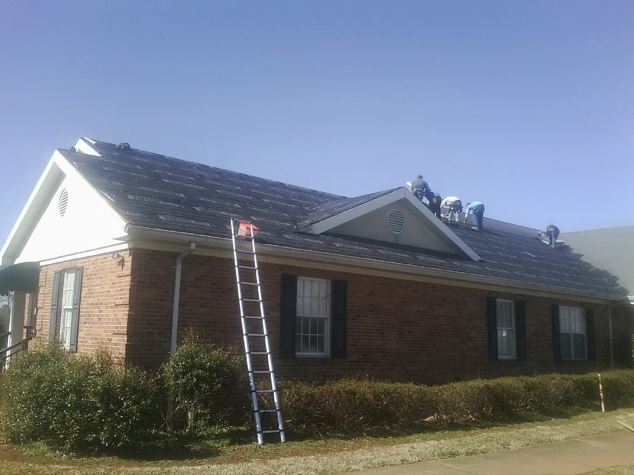 Crew tearing shingles off a brick ranch roof with a ladder set — Metal Roof Repair work by our crew in Lapaz