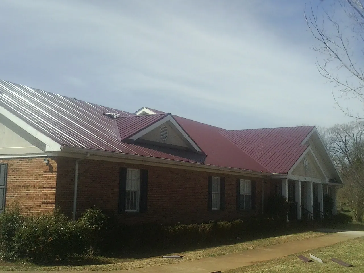 Red metal roof with gabled entries on a long brick building, from a Hail Damage Roof Repair job in Lapaz