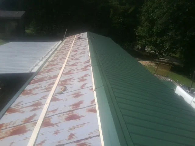 Old rusted panels beside newly installed green metal roofing — Wind Damage Roof Repair by Roofing Brothers in Lapaz