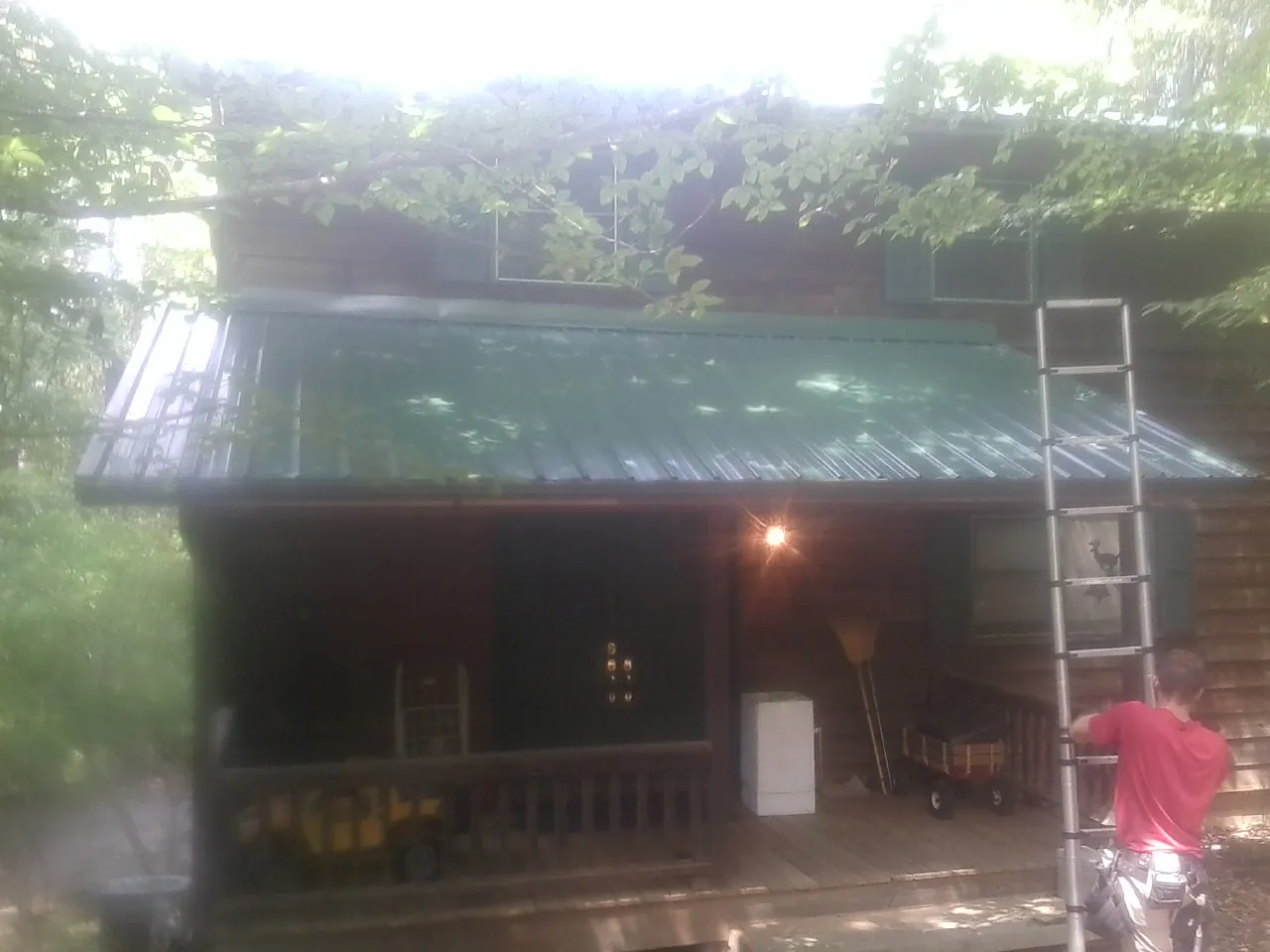 Worker on a ladder at the green porch roof of a wooded cabin in Lapaz