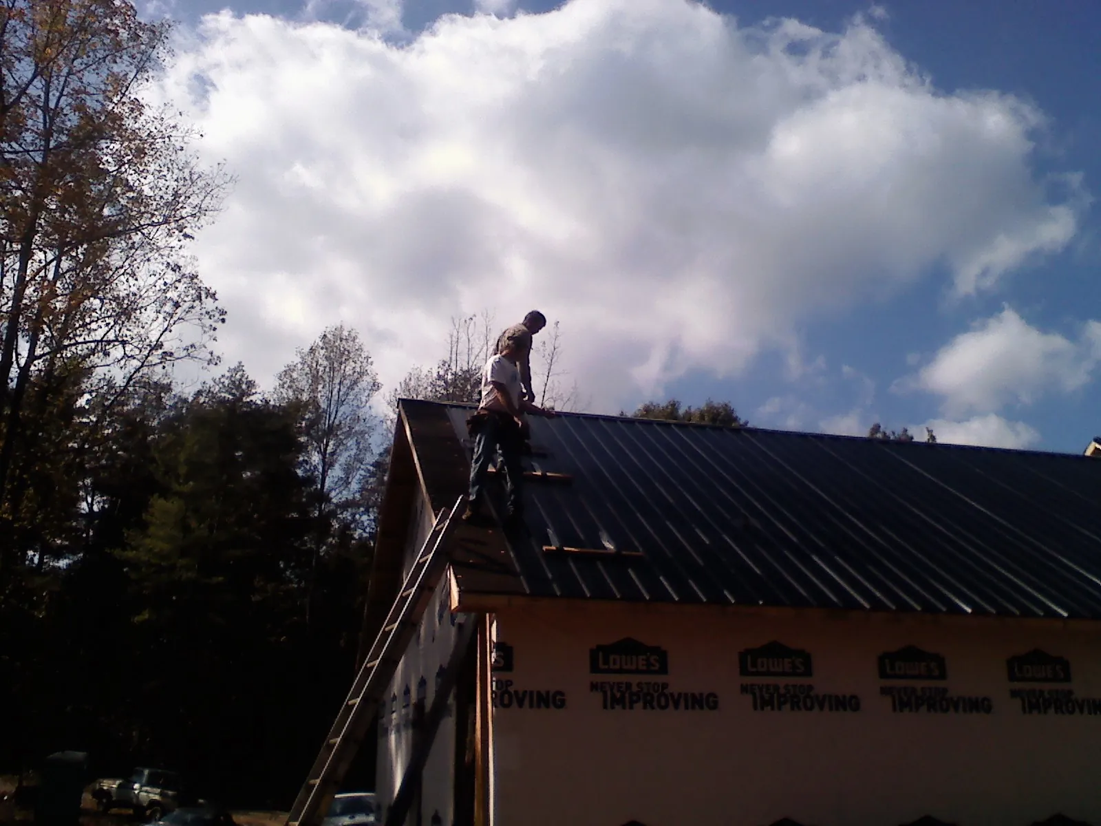 Roofer fastening dark metal panels high against a cloudy sky, from a Roof Inspection job in Lapaz